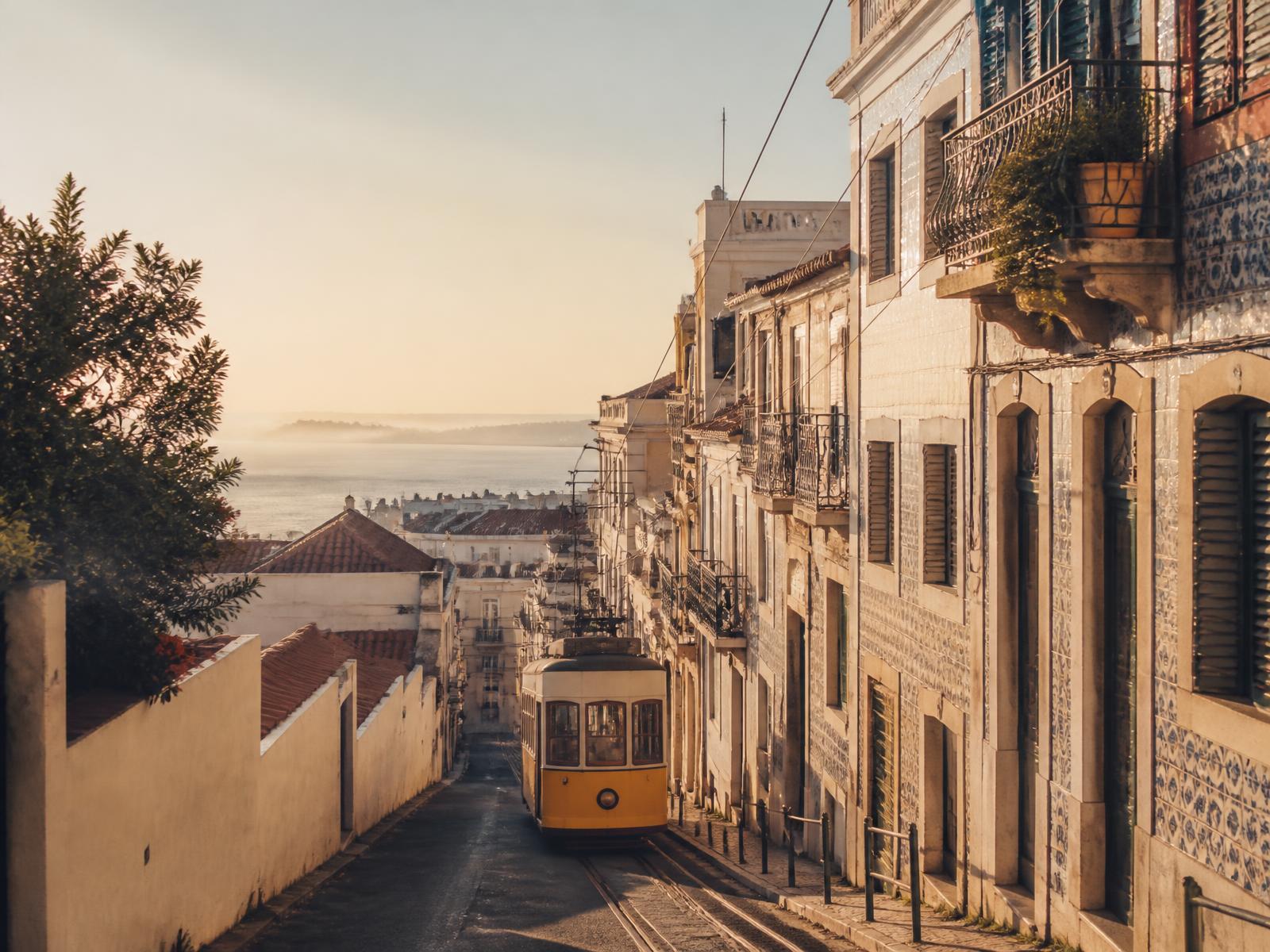 A yellow tram descending a sunlit Lisbon street toward the river